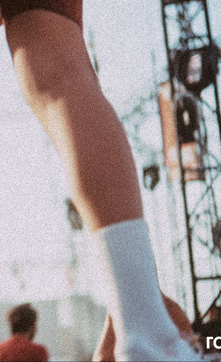 Legs and white socks in front of a festival stage rig in daylight.